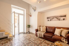 A living room with a brown leather sofa, a patterned floor, a potted plant, and a painting on the wall. - Gabbiano 2 - Sea Loft  (Bari)