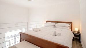 A bedroom with a wooden bed, white bedding, a bedside lamp, and a view of the outdoors. - Gabbiano 2 - Sea Loft  (Bari)