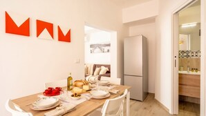 A dining area with a wooden table set for four, a refrigerator, and a view into a living space with a sofa and a painting. - Gabbiano 2 - Sea Loft  (Bari)