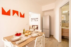 A dining area with a wooden table set for four, a refrigerator, and a view into a living space with a sofa and a painting. - Gabbiano 2 - Sea Loft  (Bari)