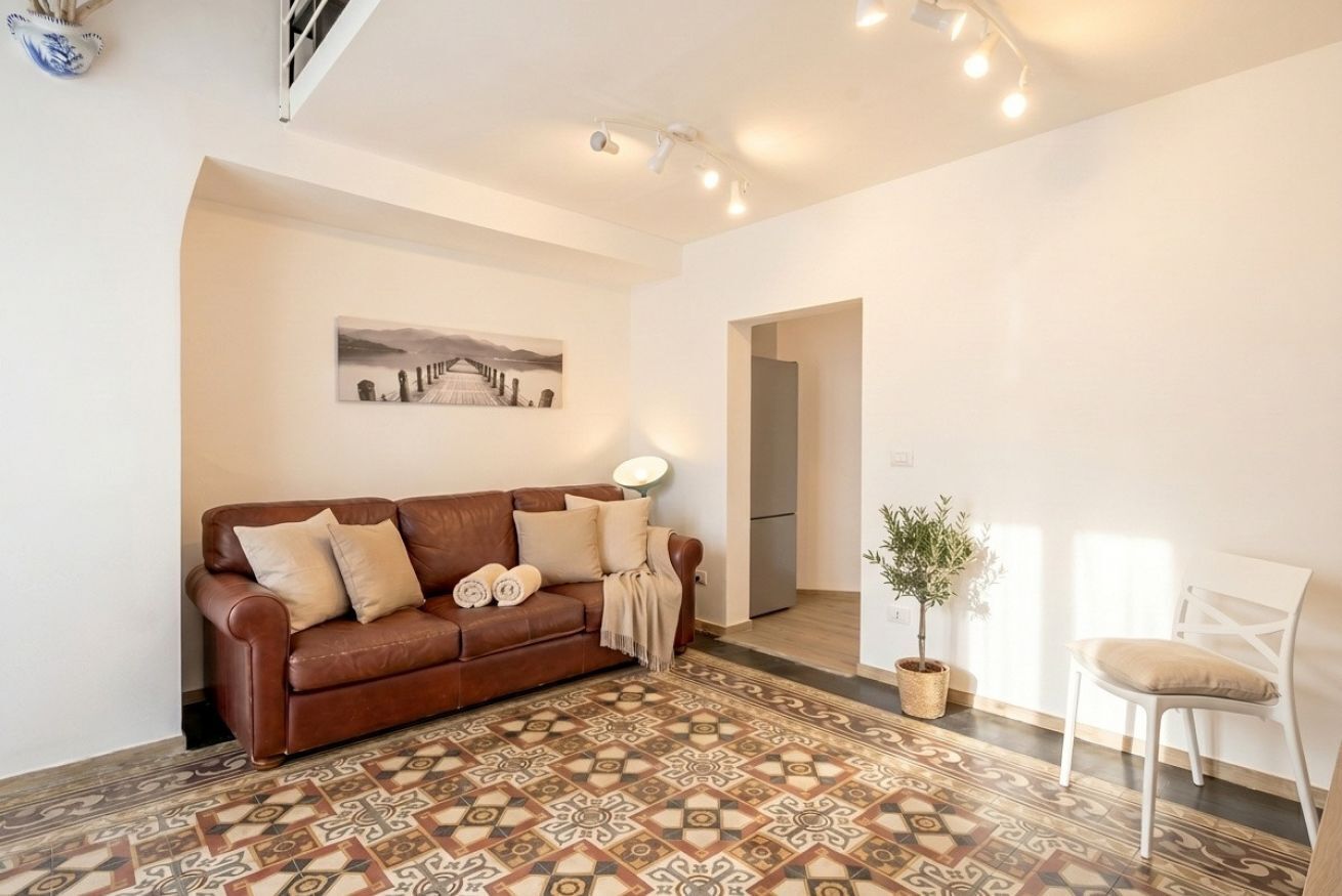 Un salon avec un sol à motifs, un canapé en cuir marron, une chaise blanche, une plante en pot et un tableau accroché au mur.