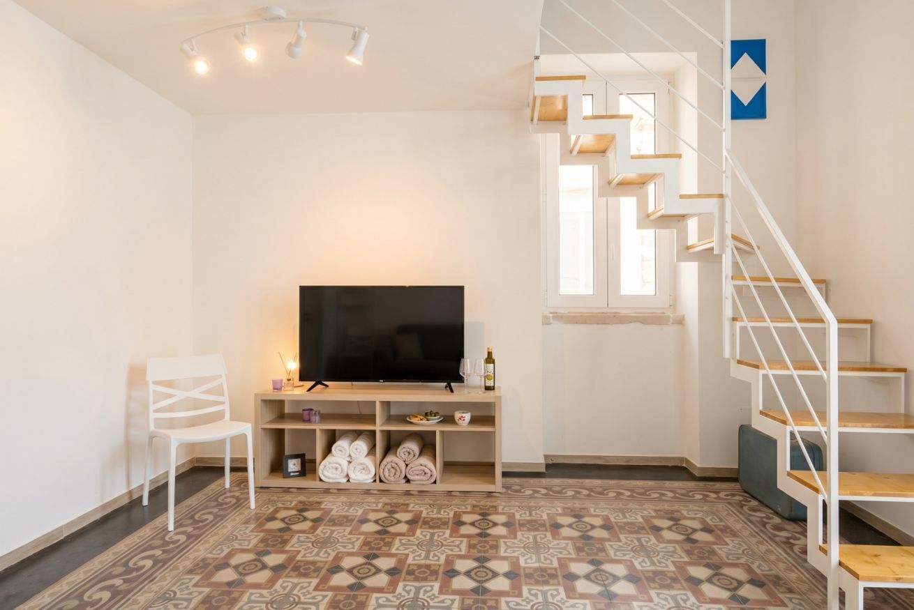 Un soggiorno moderno con una TV a schermo piatto, arredi bianchi, un pavimento decorato e una scala.