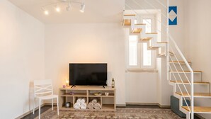 Uma sala de estar moderna com televisão de tela plana, móveis brancos, piso estampado e uma escada.