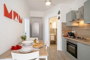 A modern kitchen with a dining area, a visible oven, and a countertop with a coffee machine. - Gabbiano 2 - Sea Loft  (Bari)