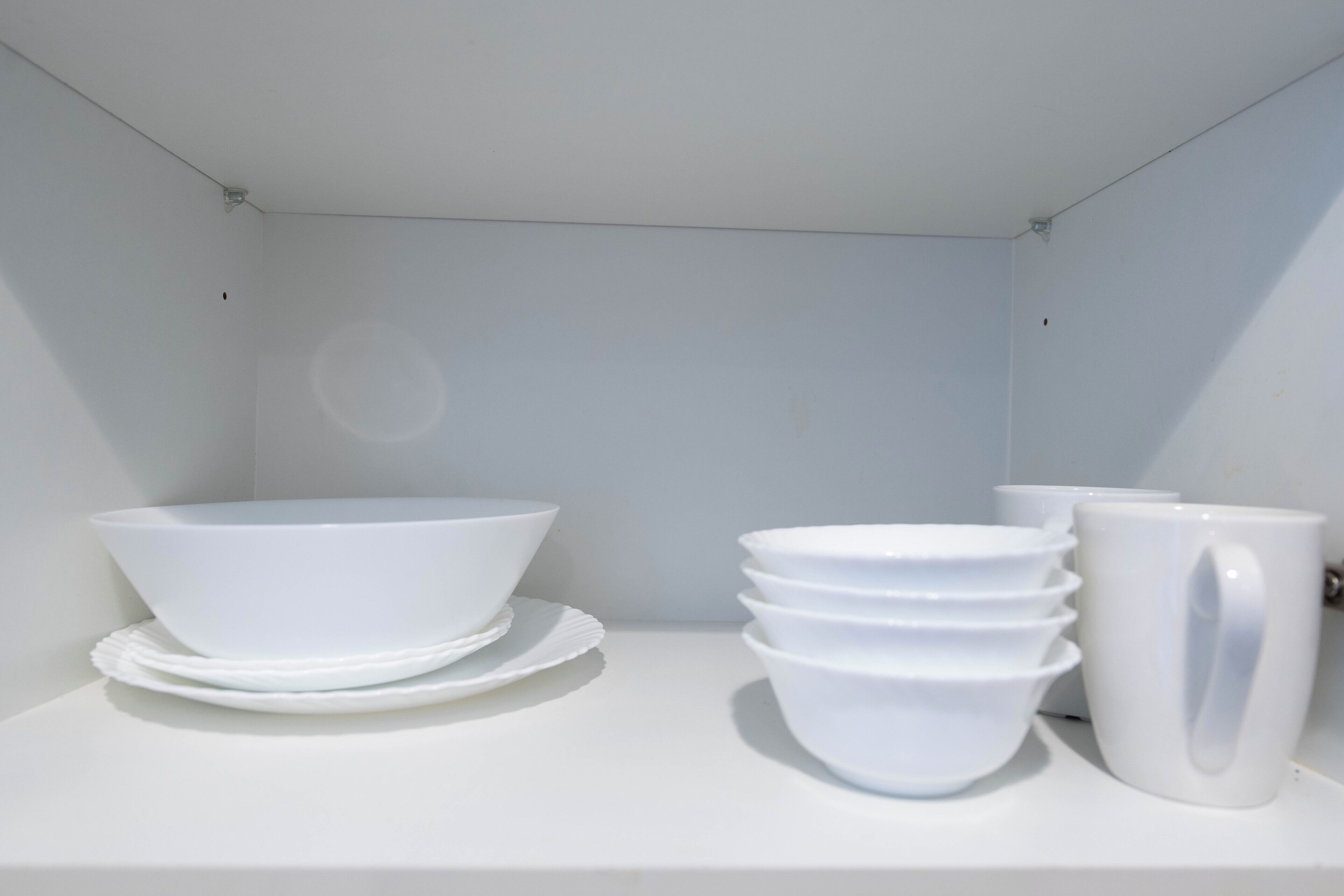 Une étagère blanche sur laquelle sont empilés des bols et des assiettes blancs, ainsi qu’une tasse blanche.