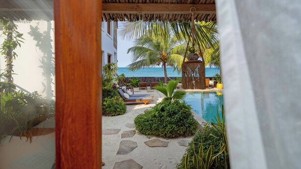 A pool area with lounge chairs and palm trees, a thatched roof structure, and a view of the ocean. - Babu Villas - Family Apartment with Sea View "Familia" (Jambiani)