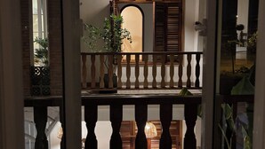A balcony with a wooden railing, a hanging light fixture, and a view of a building with a wooden door and window.
