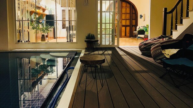 A pool area with a glass enclosure, wooden deck, and a staircase leading to an upper level.