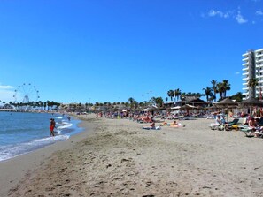 Una playa con noria, palmeras y sombrillas.
