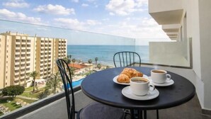 Een balkon met een tafel, stoelen, een croissant en twee kopjes koffie.