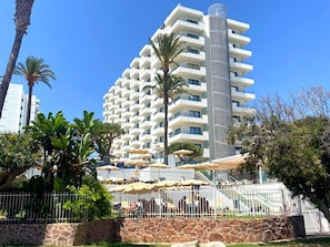 A multi-story hotel with balconies, outdoor seating, and a stone wall in the foreground.