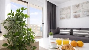 Een moderne woonkamer met een bank, een bijzettafeltje met ontbijtartikelen, een plant en uitzicht op de stad.