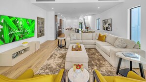 Una sala moderna con un televisor de pantalla plana grande, un sofá, una mesa de centro y un comedor con una escalera.