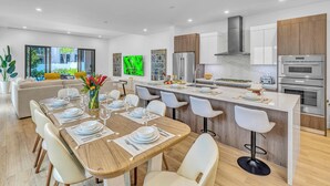Una cocina moderna con una isla central, electrodomésticos integrados y una zona de comedor con una mesa de madera y sillas blancas.