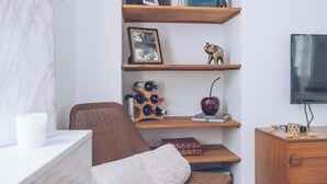 Ein modernes Wohnzimmer mit Holzboden, einem braunen Ledersessel, einer weißen gepolsterten Bank, einem Holzregal und einem Flachbildfernseher.