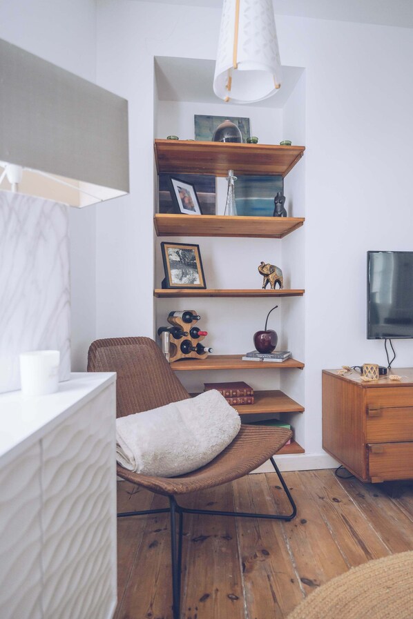 Un saló modern amb terra de fusta, una cadira de cuir marró, una banca blanca amb coixins i una prestatgeria de fusta, a més d'una televisió de pantalla plana.