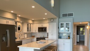 A modern kitchen with white cabinetry, stainless steel appliances, and a central island with stools. - Ma'alaea Surf, Unit A4-2 BR Ground Floor Beachfront Condo, AC, Wi-Fi, Pool (Kihei)