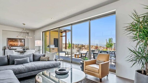 A modern living room with a sofa, armchair, and coffee table, a dining area with chairs, and a large sliding glass door leading to an outdoor patio. - Paradise Canyon-Heated Pool-Mountain View-Estate 2 (Fort Mcdowell)