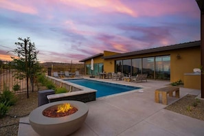 Un área de piscina moderna al aire libre con una chimenea, sillones de descanso y una vista despejada del paisaje circundante.