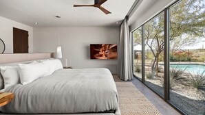 A bedroom with a bed, a ceiling fan, a TV, and a large window overlooking a pool.