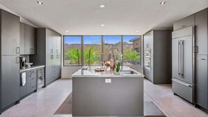 A modern kitchen with a central island, grey cabinetry, and a view of a mountainous landscape.