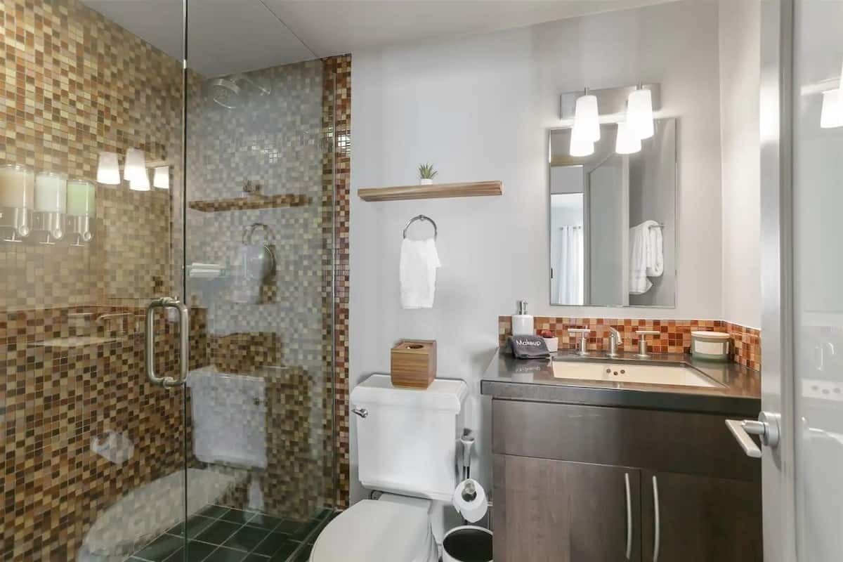 A bathroom with a glass shower enclosure, a toilet, a sink with a mirror, and a towel rack.