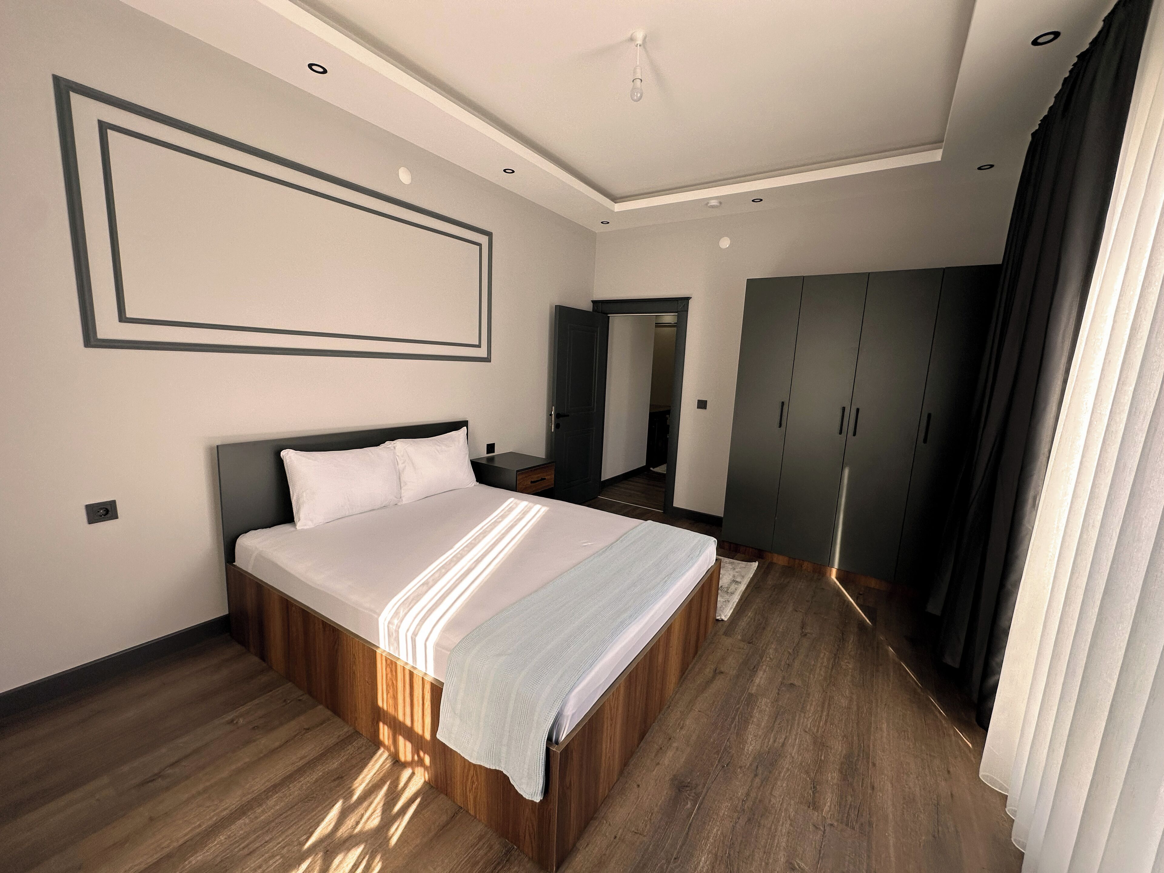 Ett modernt hotellrum med en stor säng, trägolv, en garderob och en spegel.