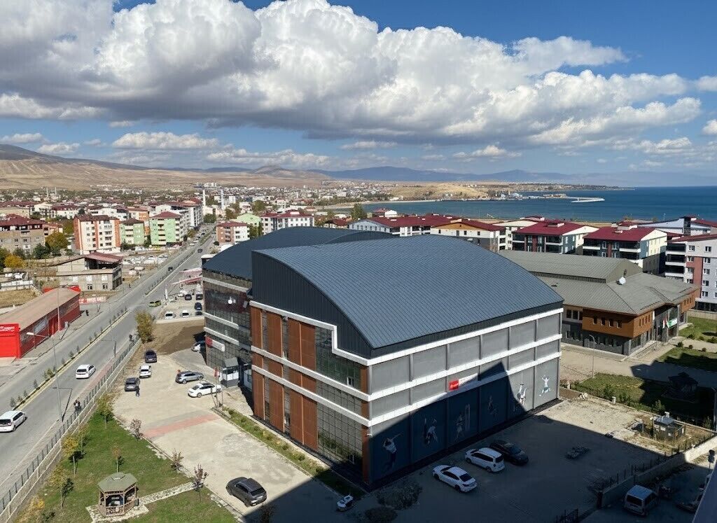 Un edificio moderno con techo curvo, rodeado de un estacionamiento y una carretera.