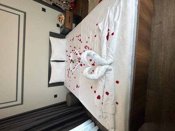 A neatly made bed with a white duvet, two pillows, and a decorative towel arrangement with rose petals.