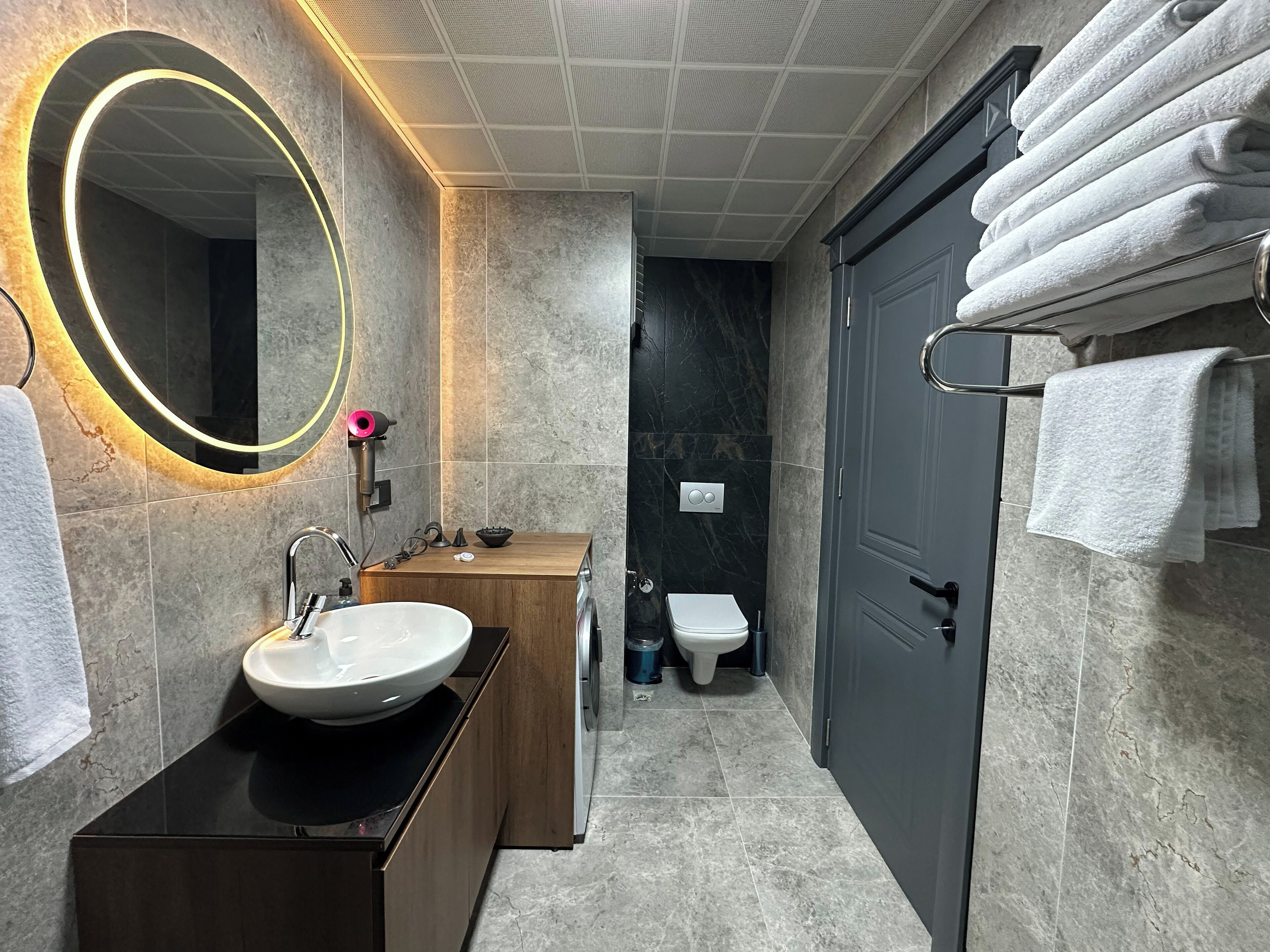 A modern bathroom with a large mirror, a sink, a toilet, and a towel rack.