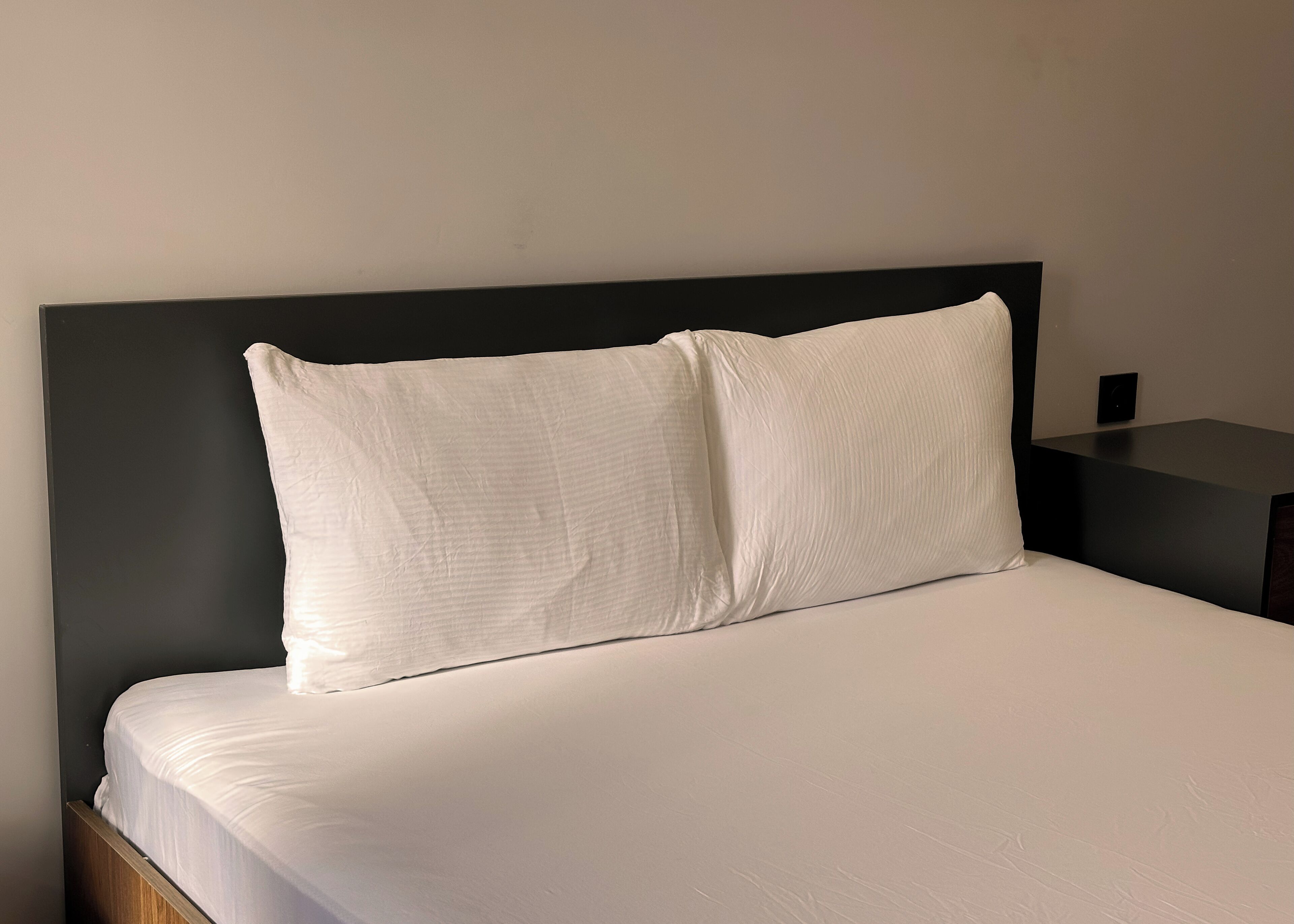Una cama con ropa de cama blanca y un cabecero negro en una habitación de hotel.