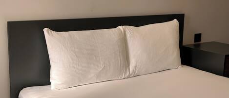 Una cama con ropa de cama blanca y un cabecero negro en una habitación de hotel.