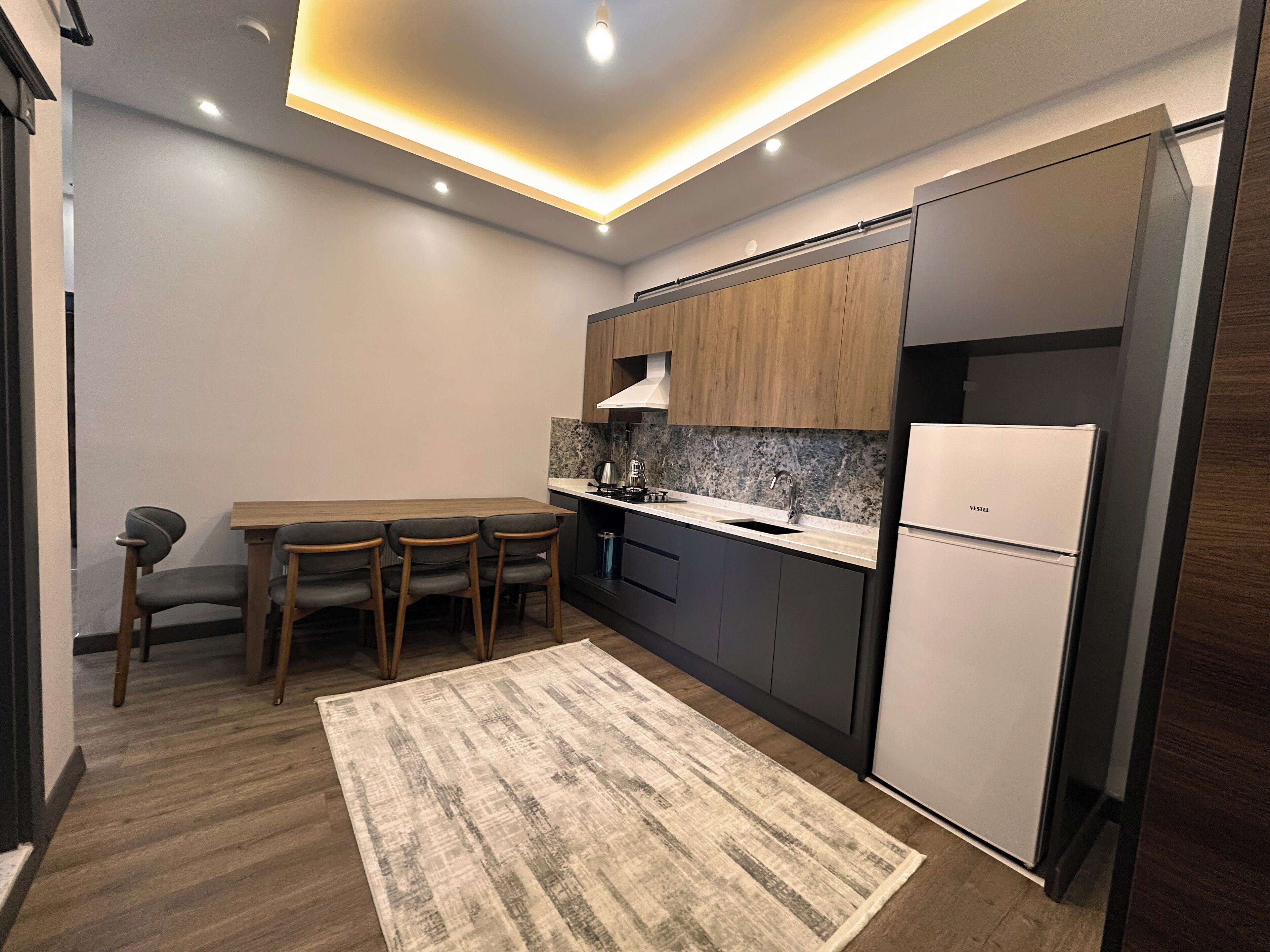 A compact kitchen with a wooden dining table, four chairs, a built-in sink, and a white refrigerator.