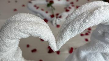 Una cama con sábanas blancas y una toalla dispuesta en forma de corazón.