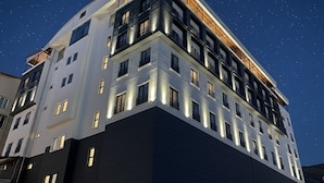Un hotel de varios pisos con diseño moderno, que destaca por su estructura en esquina y ventanas iluminadas.