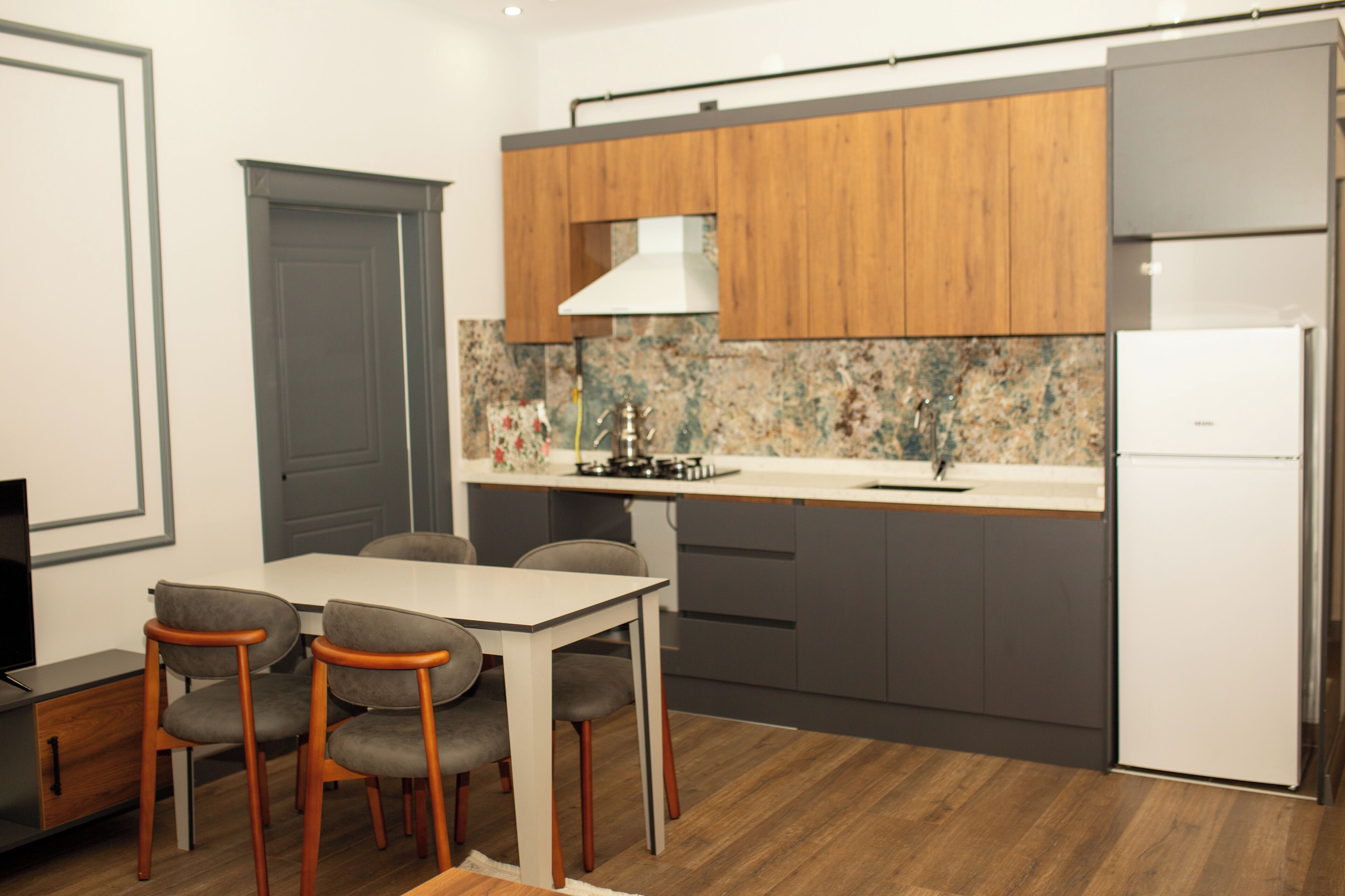 A compact kitchen with a dining area, wooden cabinets, a white refrigerator, and a tiled backsplash.