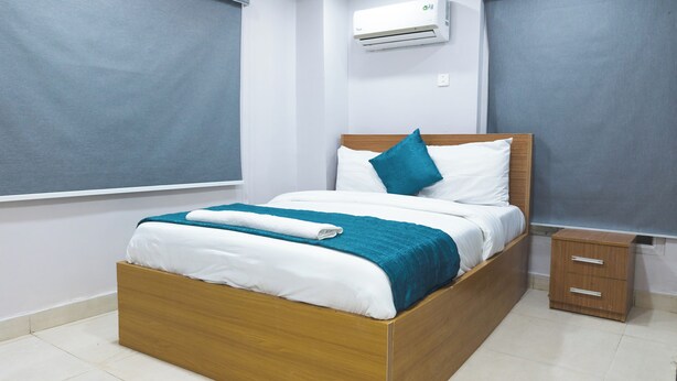 A neatly made bed with a wooden frame, white bedding, and a teal throw blanket. - Single Room in Secure Apartment – Akoka Yaba Lagos (Yaba)