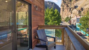 A balcony with a wooden railing, a black chair, and a view of a town with buildings and a mountain in the background.