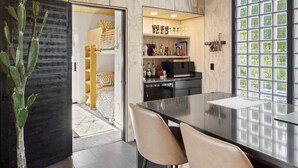 A modern kitchen with a dining area, wooden cabinets, and a large window with a view of greenery.