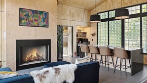 A modern interior with a fireplace, a dining area with bar stools, and a large window with a view.
