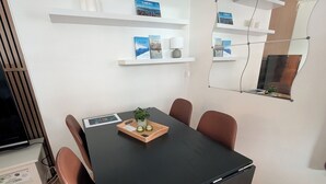 Een moderne eetruimte met een zwarte tafel, bruine stoelen en een klein plantenarrangement. Witte schappen met decoratieve objecten en een spiegel sieren de muren.