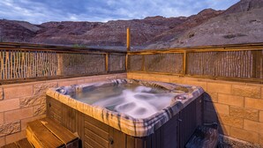 Un bain à remous à l’extérieur en bois, entouré d’une clôture en bois et de murs en briques, avec une chaîne de montagnes en toile de fond.
