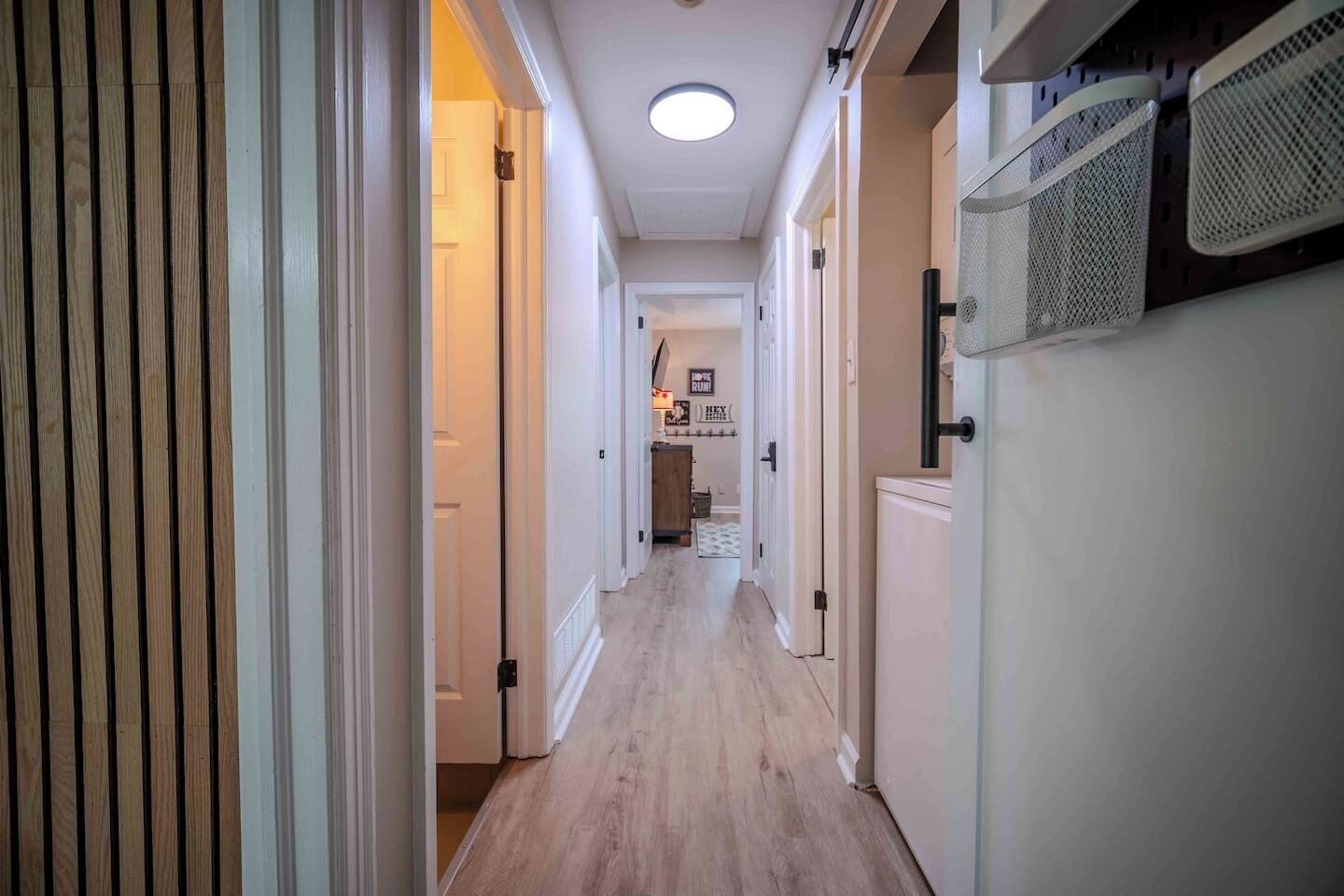 A hallway with wooden flooring, white walls, and a ceiling light.