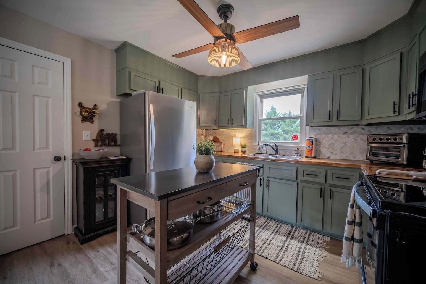 A kitchen with a refrigerator, oven, and a ceiling fan.