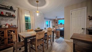Un comedor con una mesa y sillas de madera, una lámpara colgante y vista a la cocina.