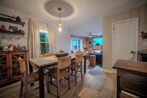 Un coin repas avec une table et des chaises en bois, un luminaire suspendu et une vue sur la cuisine.