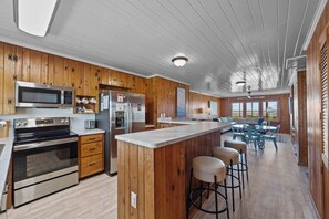 A modern kitchen with wooden paneling, stainless steel appliances, and a central island with bar stools. - Holliday Haven #200 - Oceanfront Escape in Topsail Beach, Sleeps 9! (Topsail Beach)