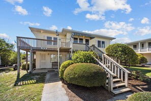 A two-story house with a porch, a staircase, and a well-maintained lawn. - Holliday Haven #200 - Oceanfront Escape in Topsail Beach, Sleeps 9! (Topsail Beach)