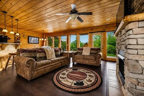 A cozy living room with a fireplace, leather sofas, a round rug, and a ceiling fan.