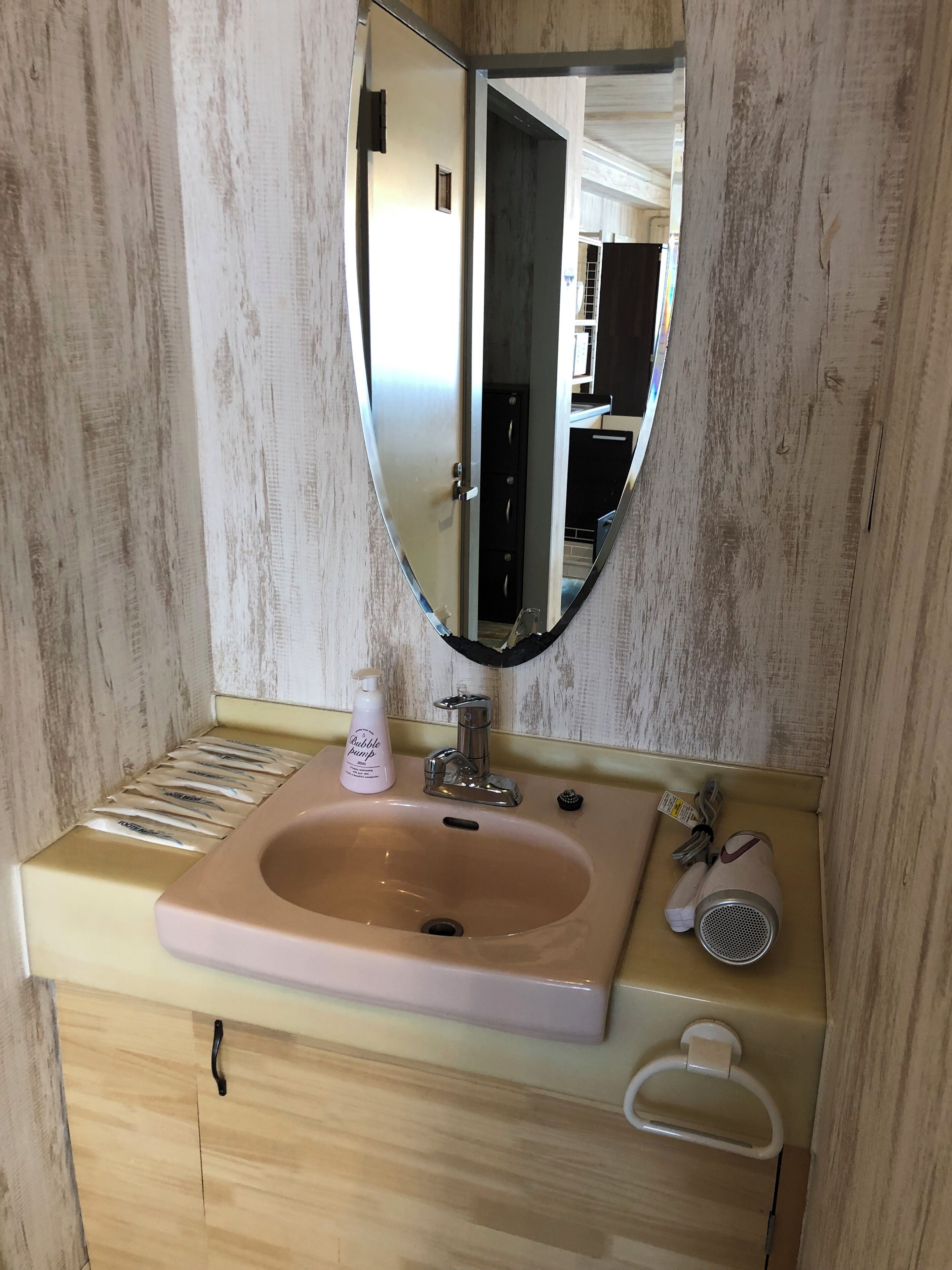 A bathroom with a wooden vanity, a pink sink, a mirror, and a handheld showerhead.